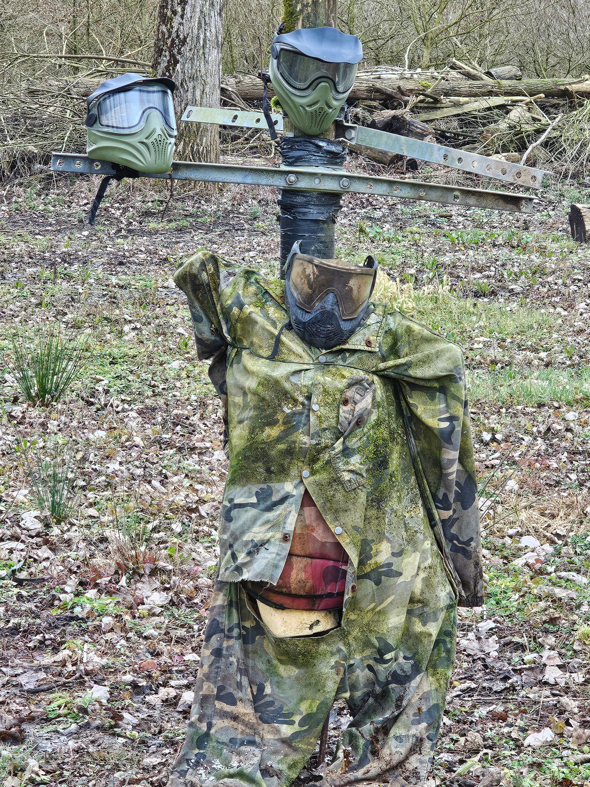 Cible de paintball : vêtements de camouflage sur un poteau, deux masques de paintball, décor forestier.