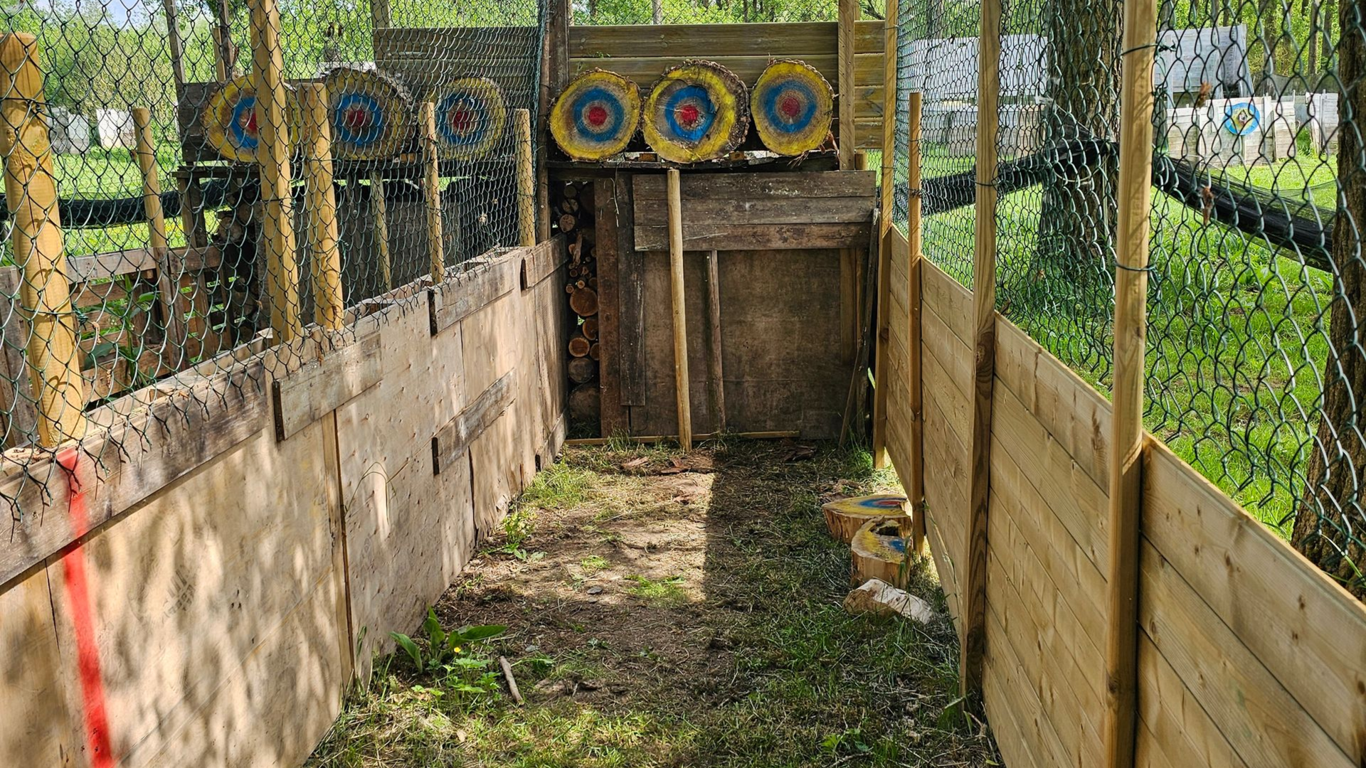 Terrain de tir à l'arc avec cibles en bois, clôture de sécurité et chemin d'accès.