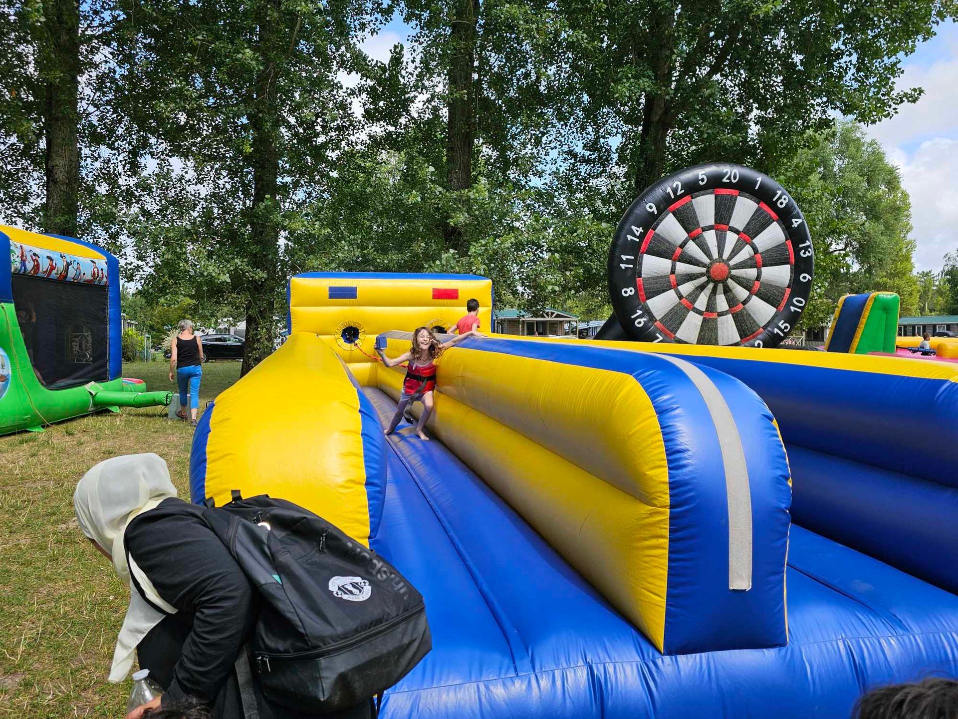 Enfant glissant sur un parcours d'obstacles gonflable ; cible de fléchettes à la fin, en extérieur.