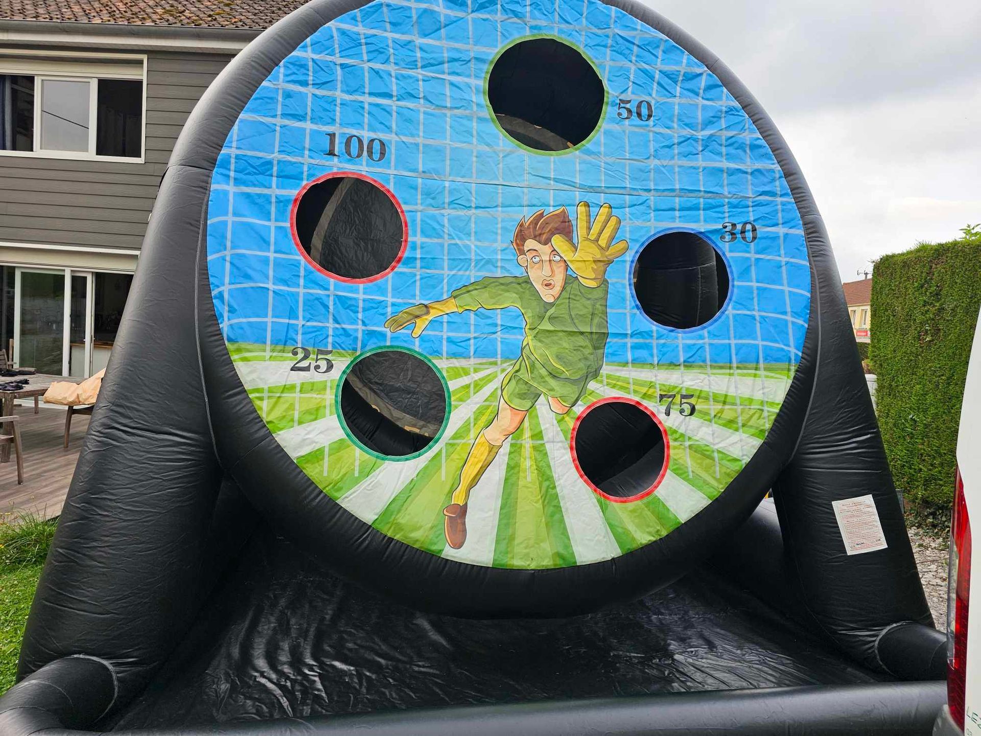 Jeu de cible de football gonflable avec un gardien de but, des trous numérotés et un cadre noir, à installer à l'extérieur.