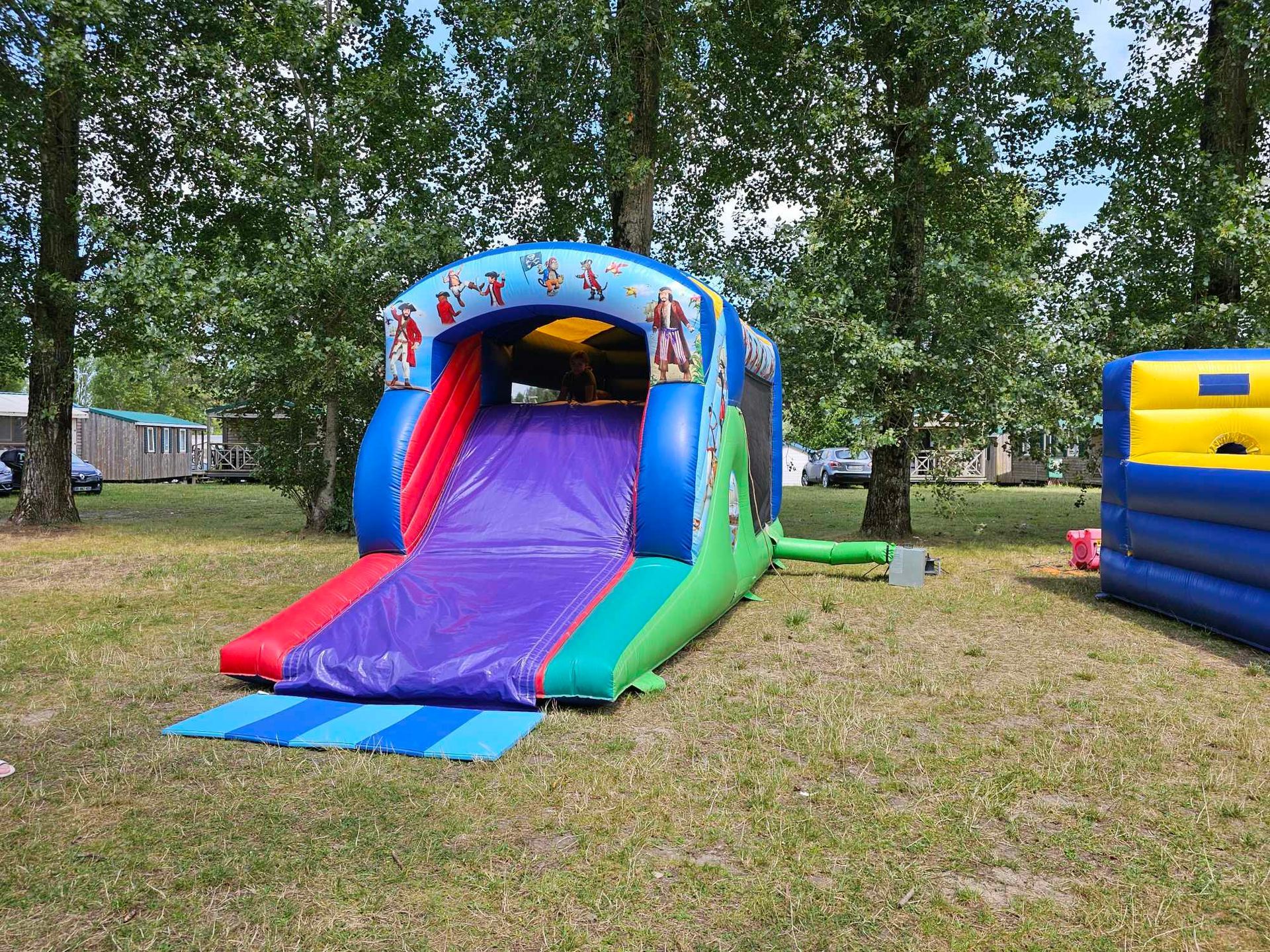 Toboggan gonflable coloré sur l'herbe ; arbres en arrière-plan.