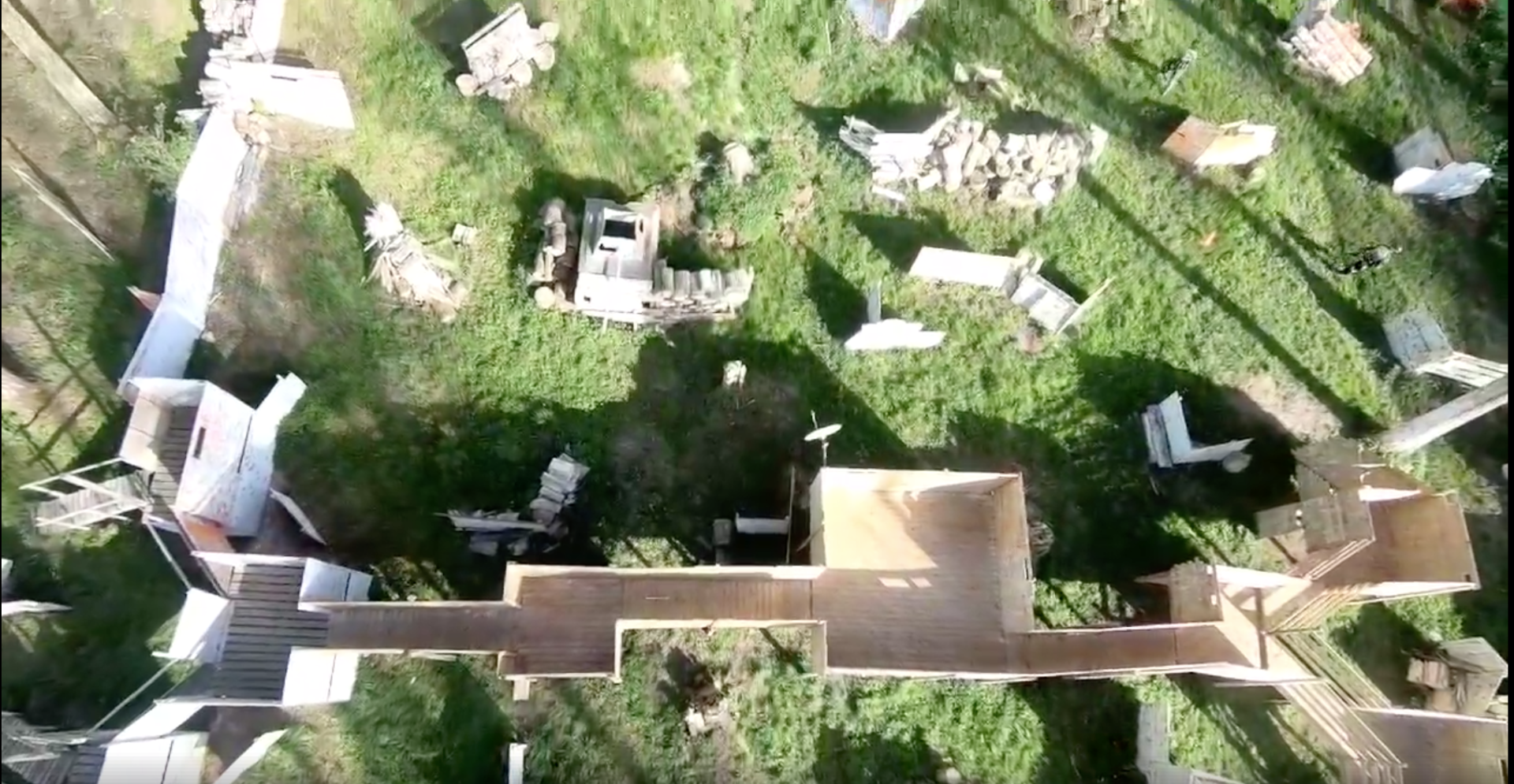 Vue aérienne d'un terrain de paintball extérieur avec des structures en bois, des zones herbeuses et des débris épars.