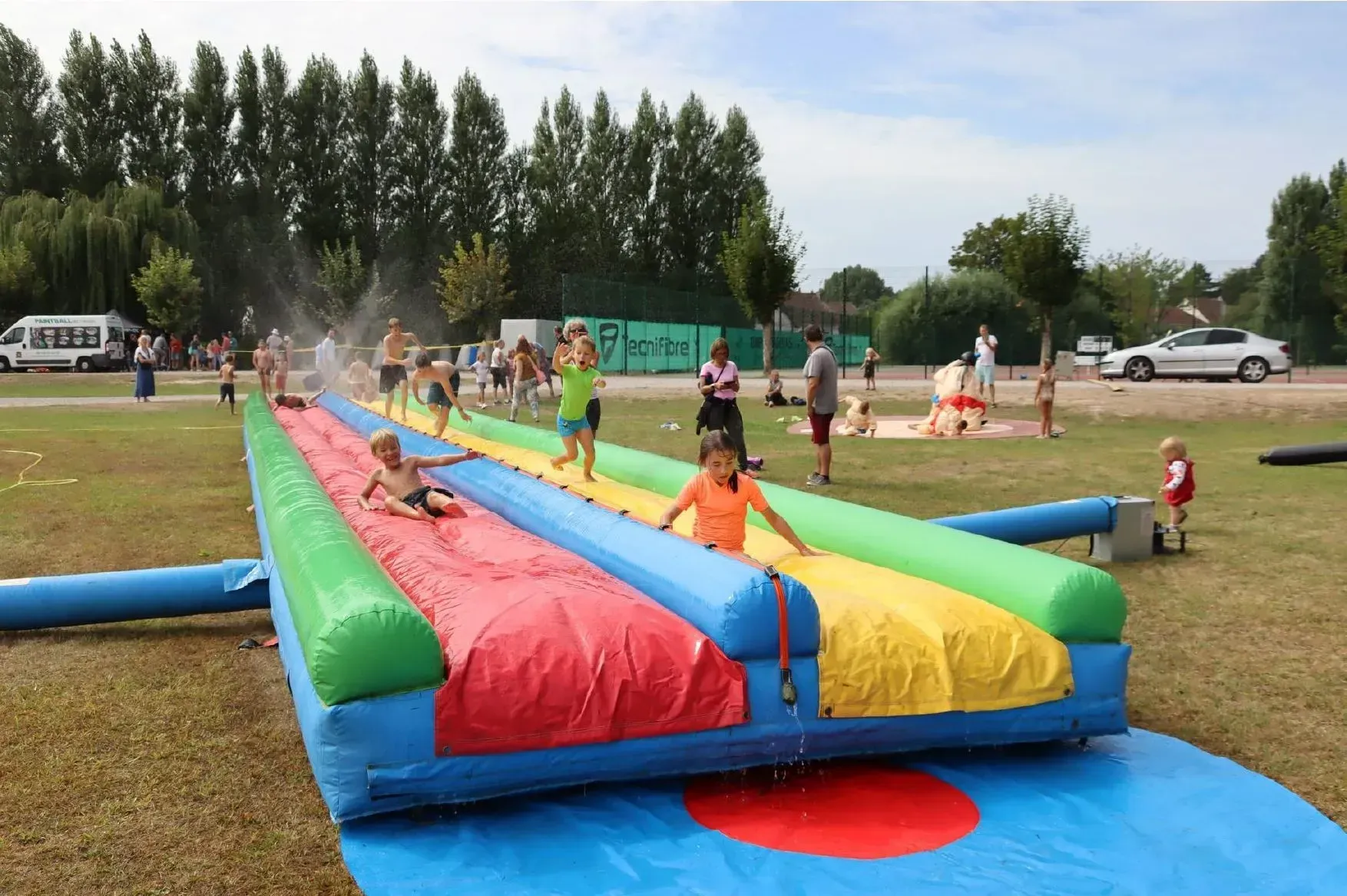 Des enfants jouent sur un toboggan aquatique gonflable coloré à l'extérieur. L'eau jaillit le long du toboggan.