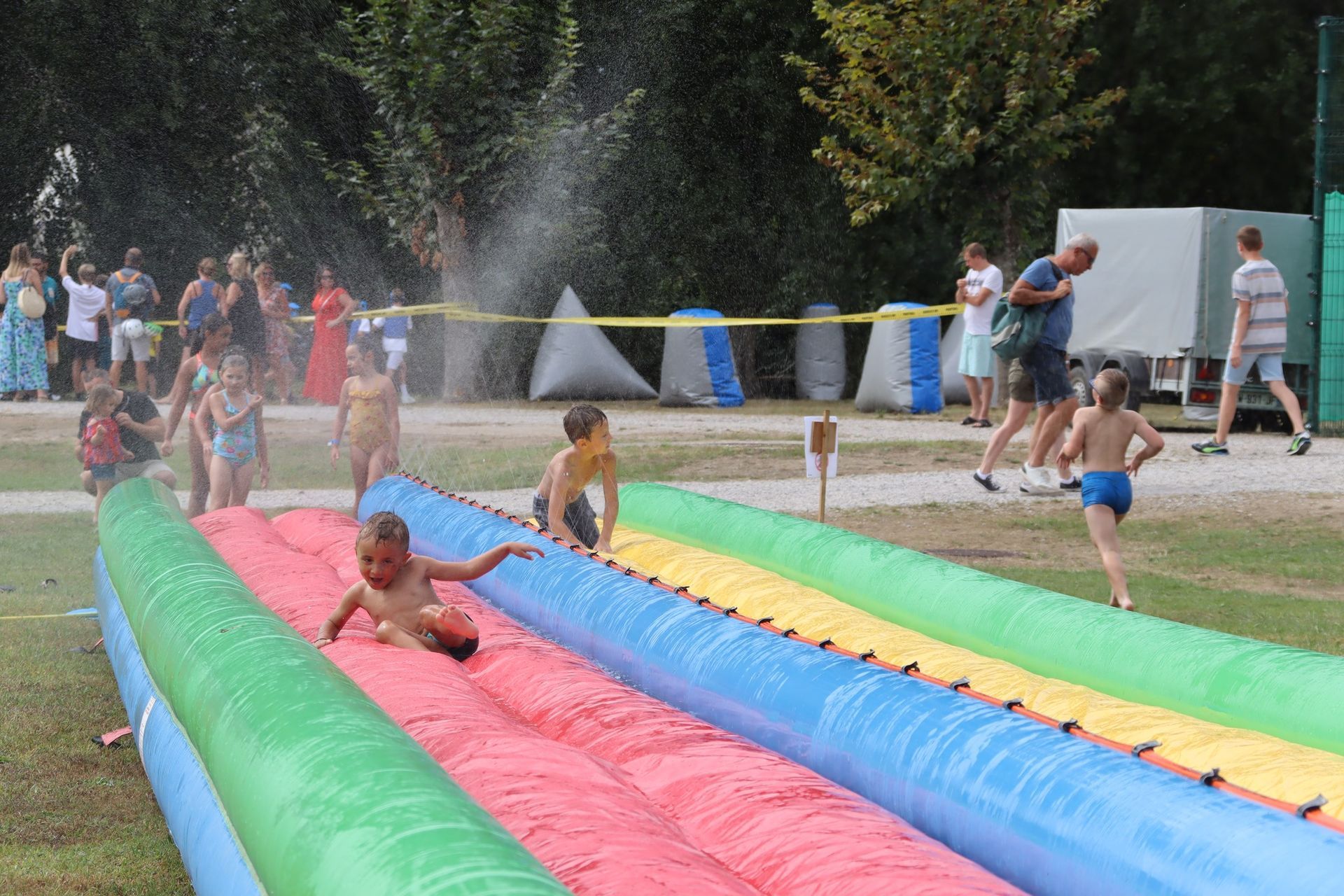 Des enfants jouent sur un toboggan aquatique coloré, sous les jets d'eau d'un parc.
