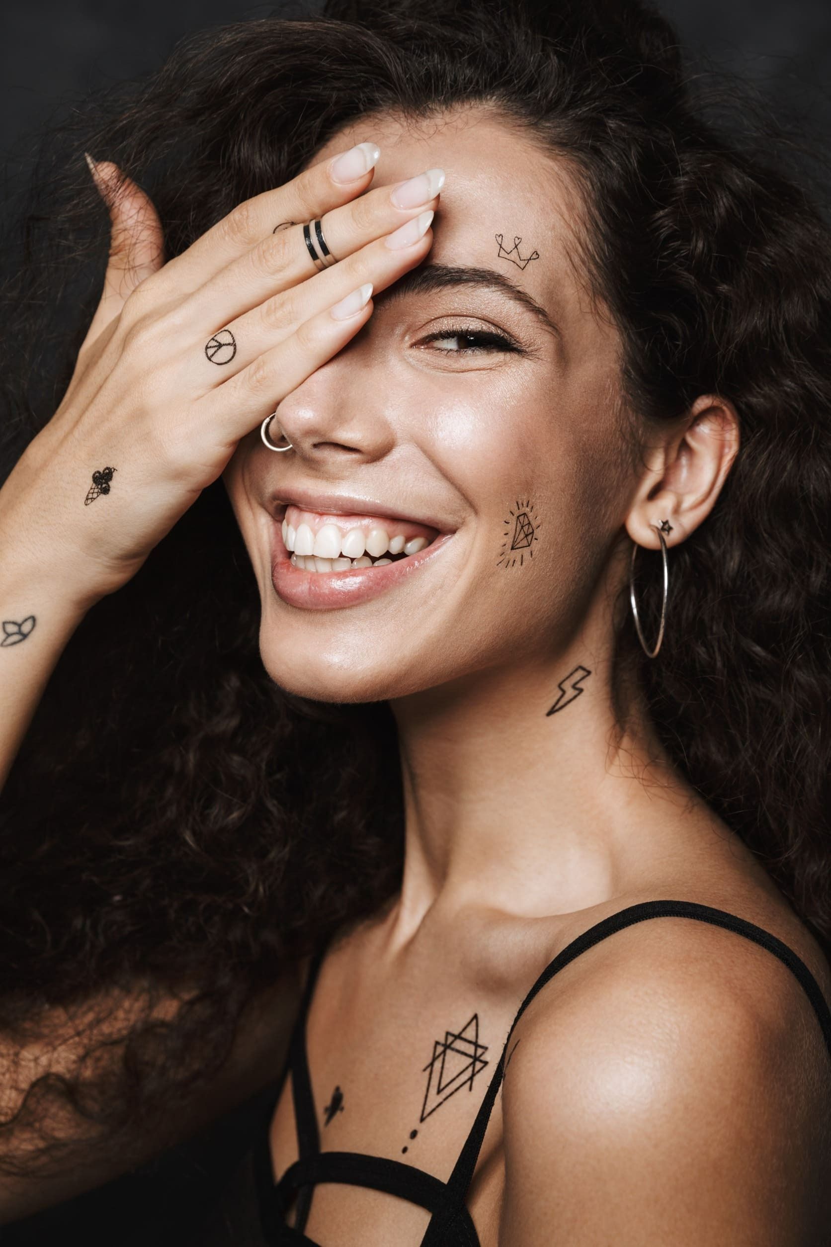 Una mujer con tatuajes en la cara sonríe y se cubre la cara con la mano.