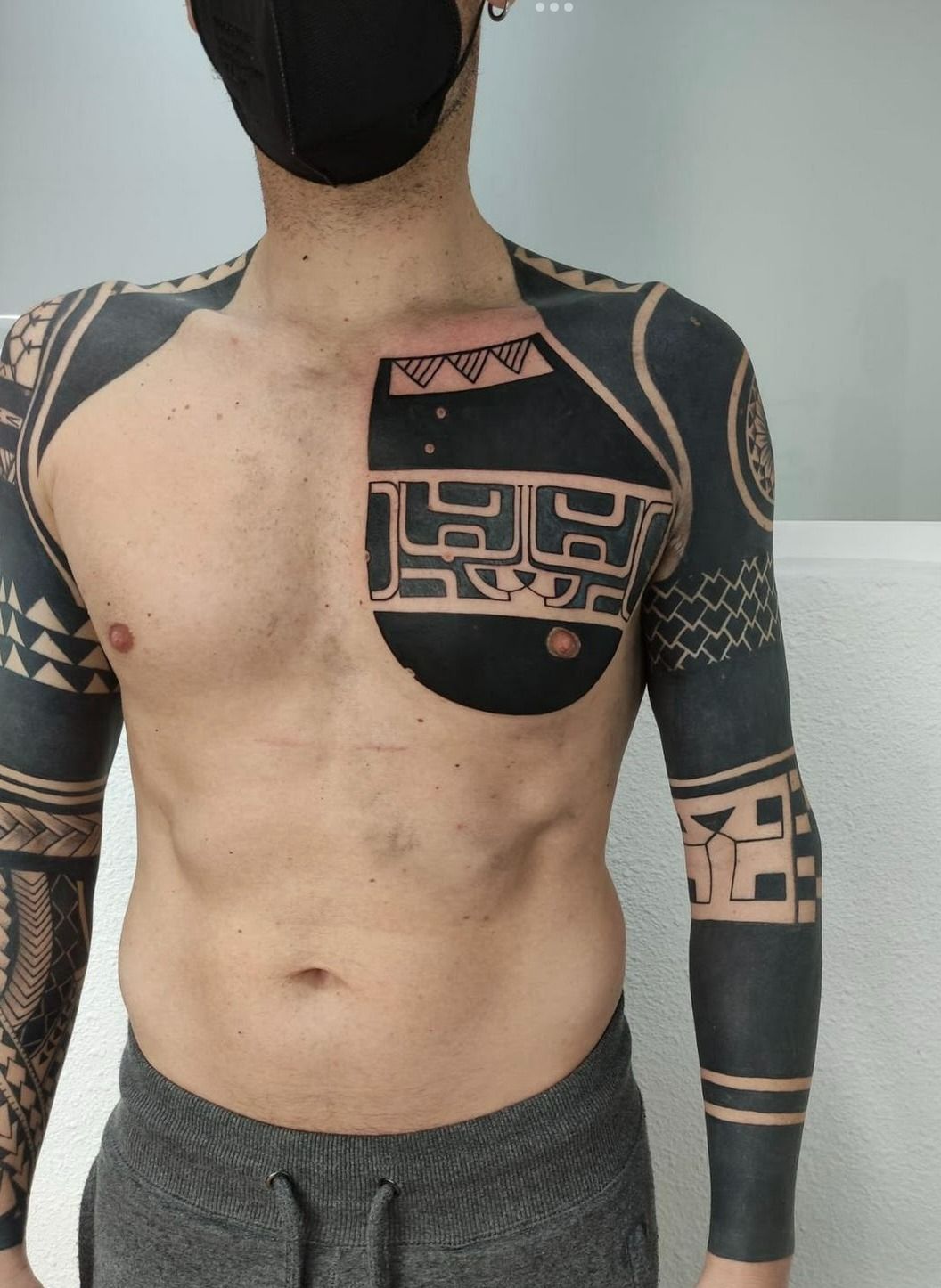 Un hombre con un tatuaje en el pecho y las mangas lleva una máscara.