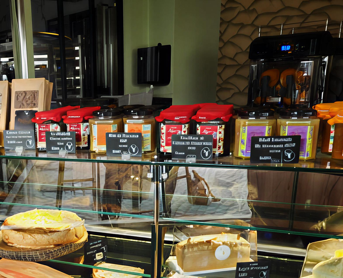 Une vitrine de boulangerie présentant des rangées de bocaux à couvercles rouges sur des étagères surplombant divers gâteaux et pâtisseries.