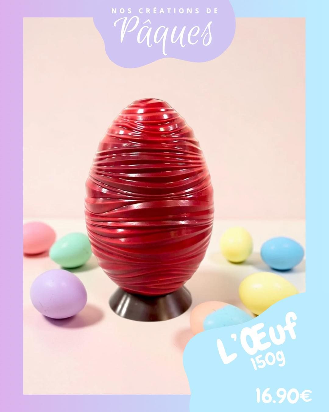 Un œuf de Pâques en chocolat rouge texturé sur un socle, entouré de petits œufs aux couleurs pastel, au prix de 16,90 € pour 150 g.