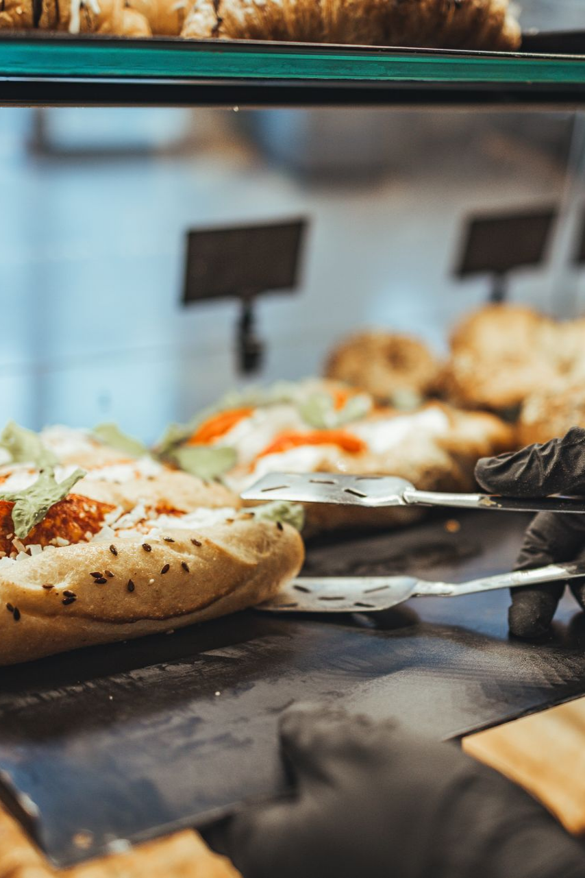 Gros plan sur une main gantée utilisant des pinces métalliques pour servir un sandwich garni à un comptoir de restauration.