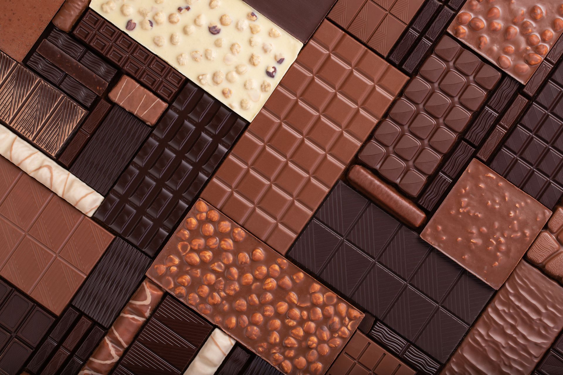 Vue à plat de différentes tablettes de chocolat, notamment des variétés de chocolat noir, au lait et blanc, avec des noix et différentes textures.