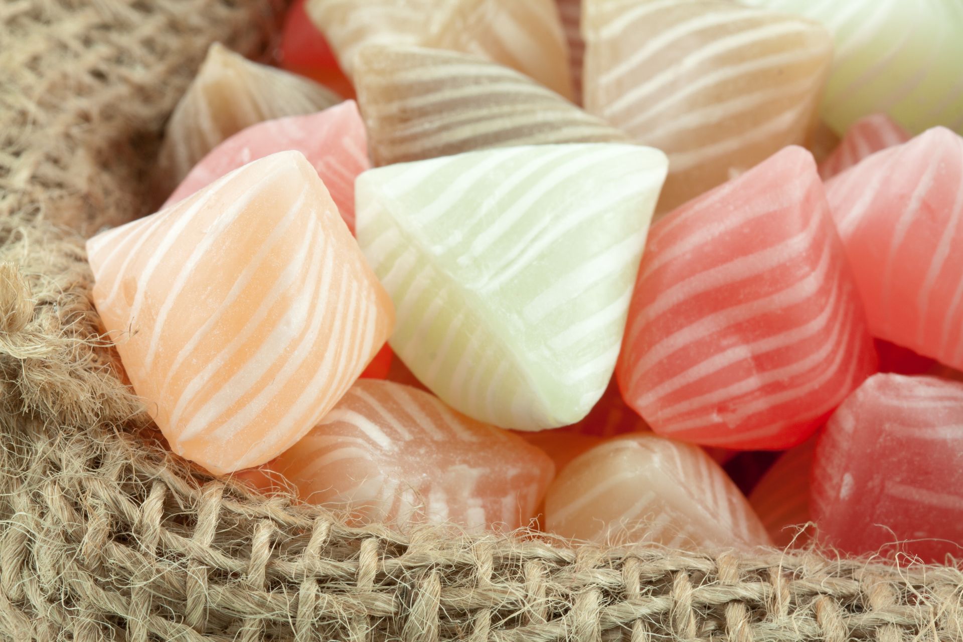 Gros plan sur des bonbons durs triangulaires, colorés et rayés, entassés dans un sac de jute.