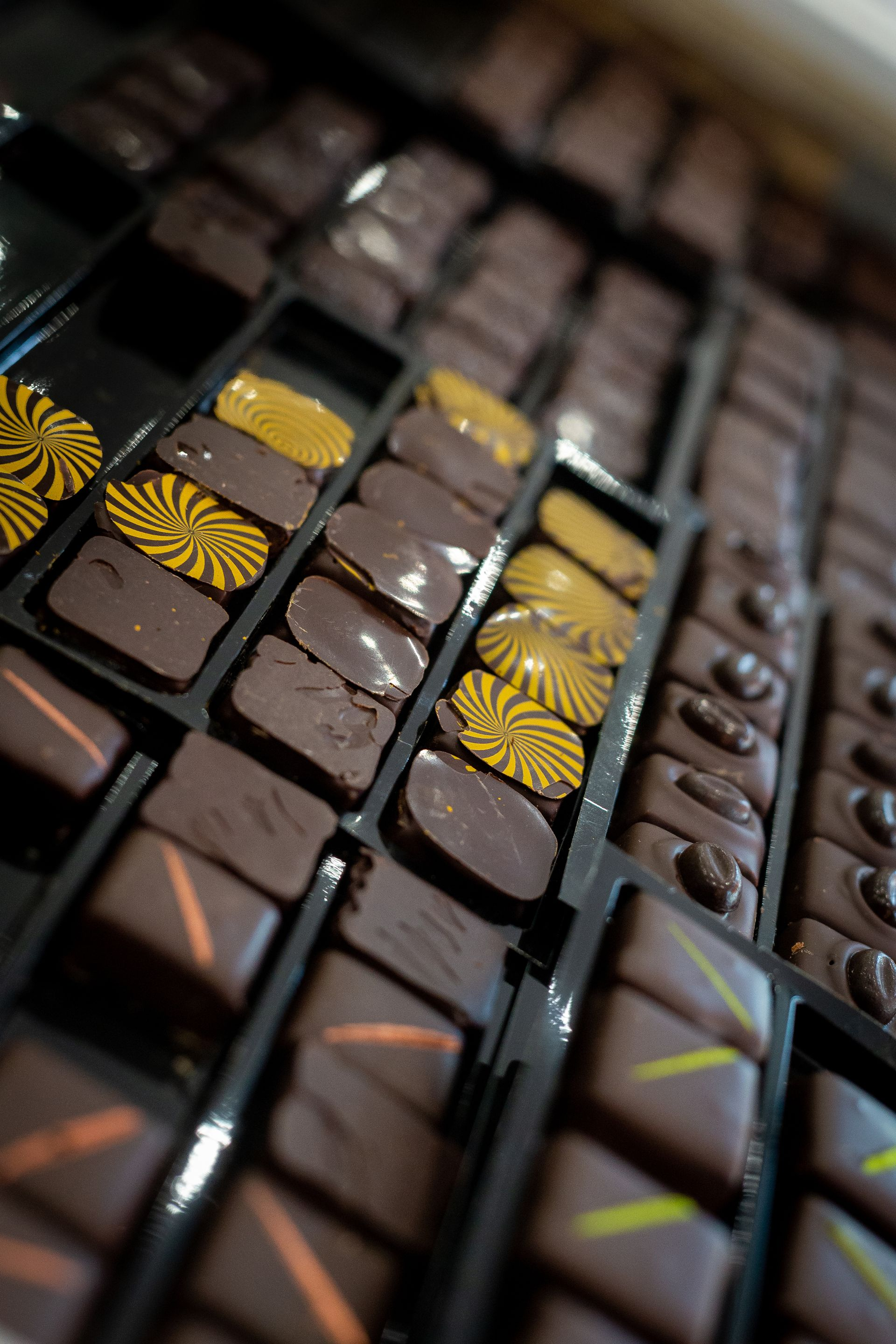 Un plateau garni de rangées de chocolats artisanaux assortis, présentant des formes variées, des textures onctueuses et des motifs divers.