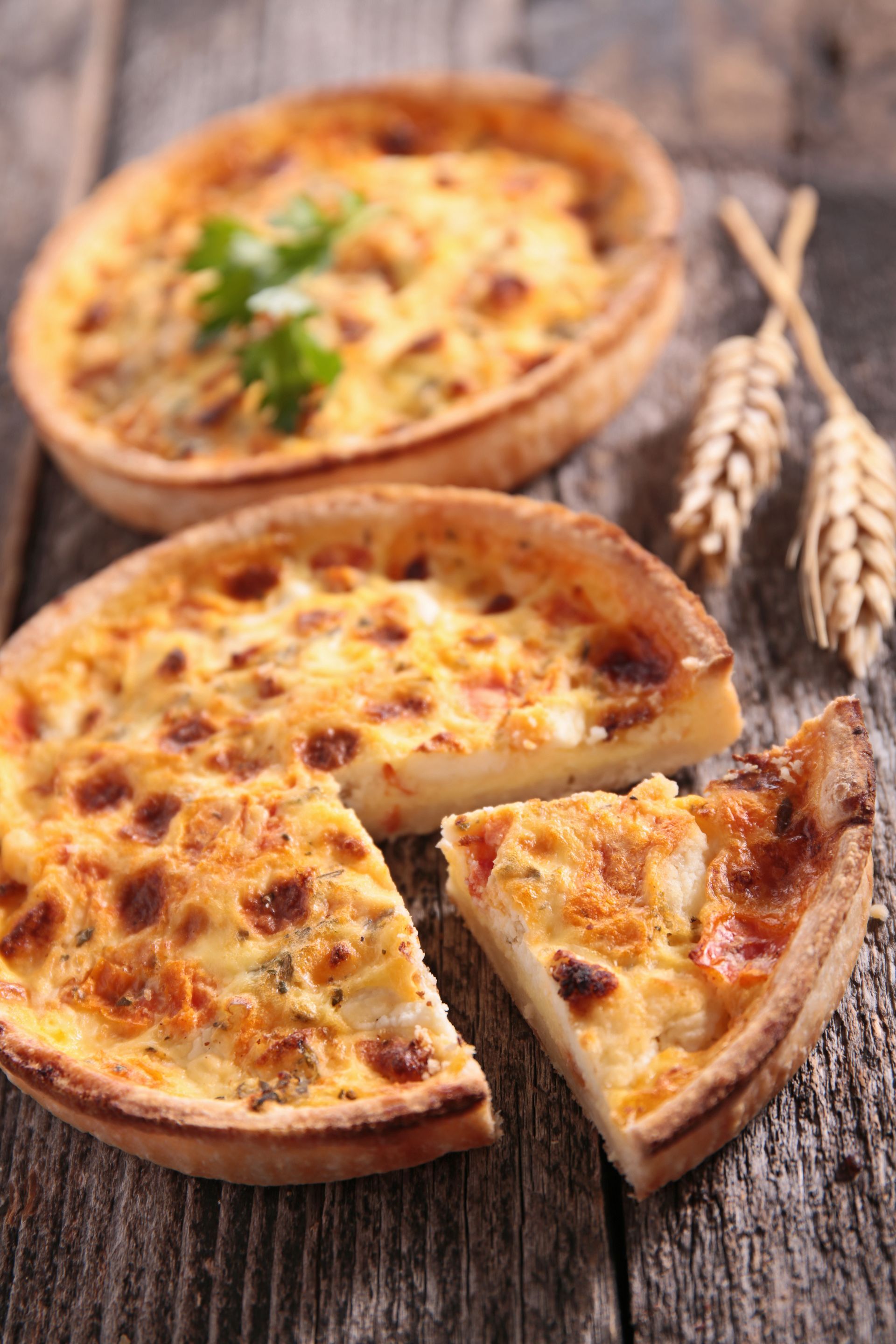 Deux quiches dorées et fraîchement cuites sont posées sur une table rustique en bois, une part étant coupée de la quiche au premier plan.