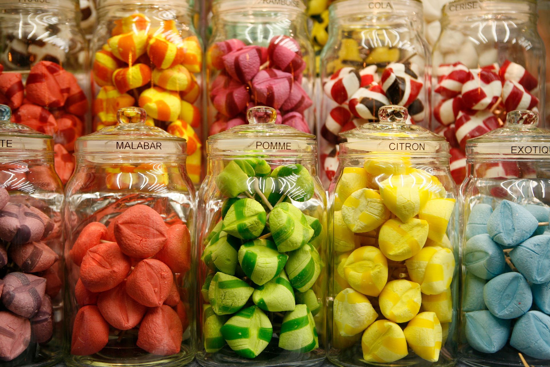 Des rangées de bocaux en verre remplis de bonbons durs colorés aux formes originales sur les étagères d'un magasin.