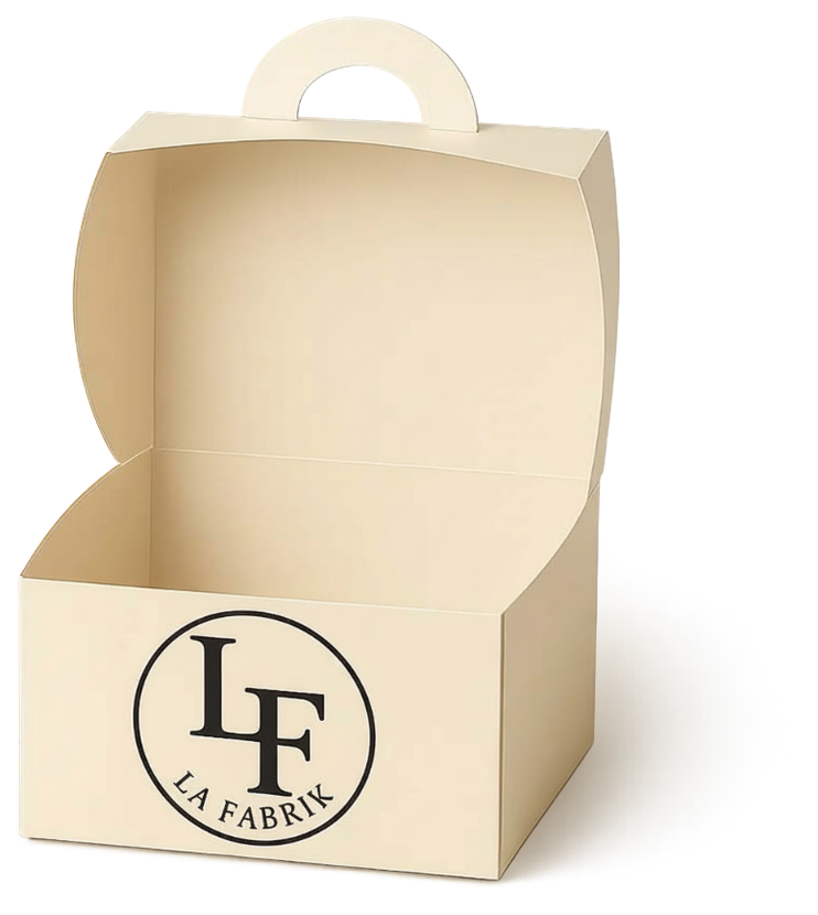 Une boîte en carton ouverte, de couleur crème, avec une poignée et un logo rond LF LA FABRIK sur le devant.