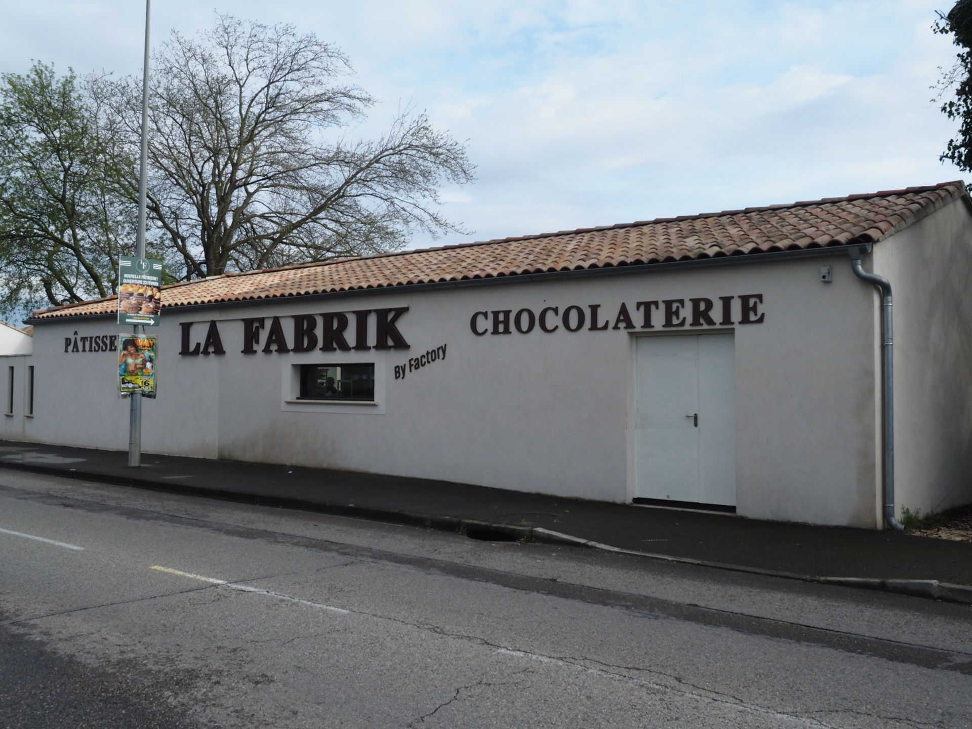 Un bâtiment long et bas, de couleur beige, avec un toit de tuiles et l'enseigne LA FABRIK CHOCOLATERIE sur le mur extérieur.