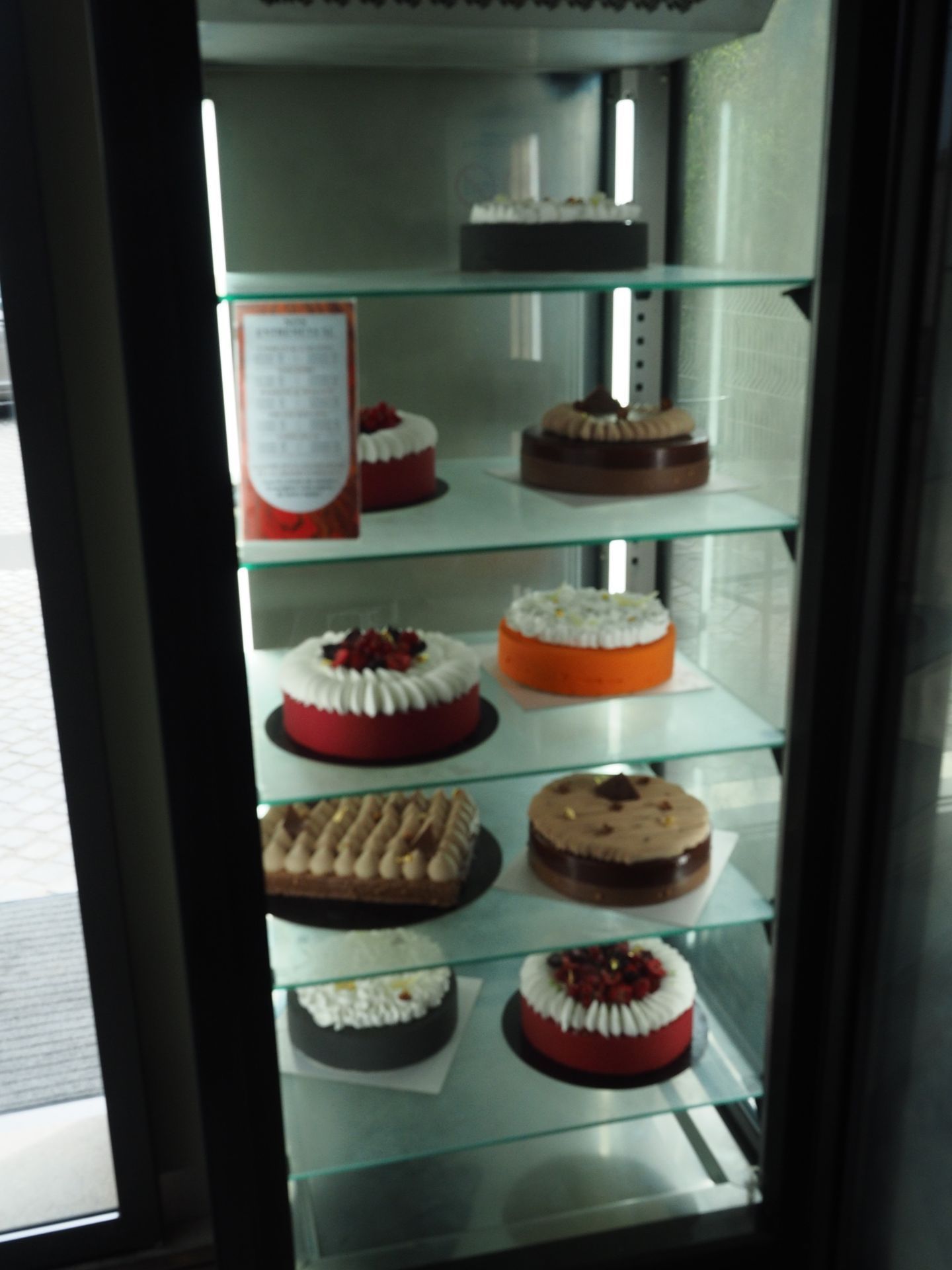 Une vitrine réfrigérée en verre présentant plusieurs gâteaux ronds et rectangulaires sur cinq étagères.