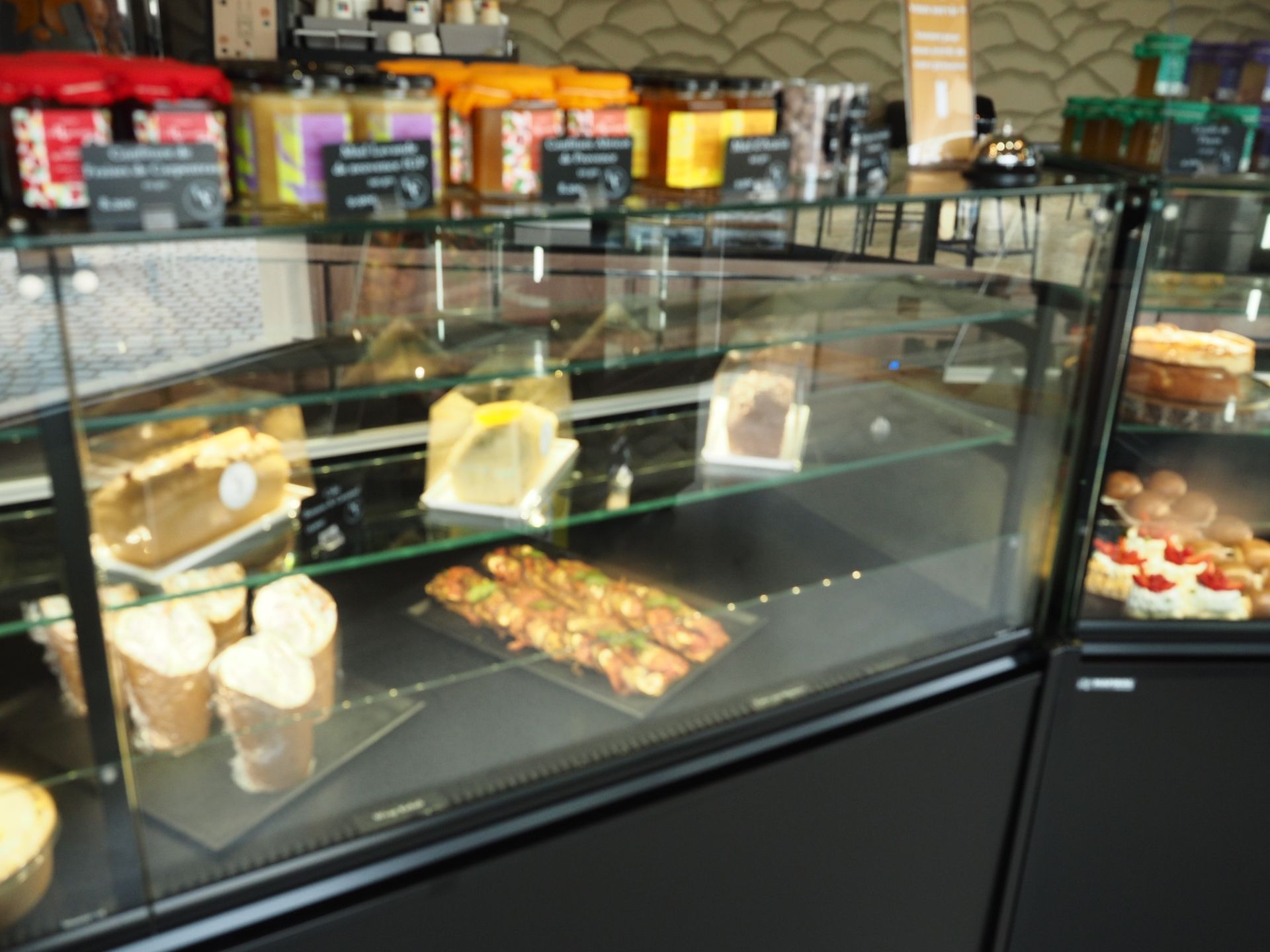 Une vitrine de boulangerie remplie de gâteaux, de pâtisseries et de bocaux de confitures variés sur les étagères supérieures.
