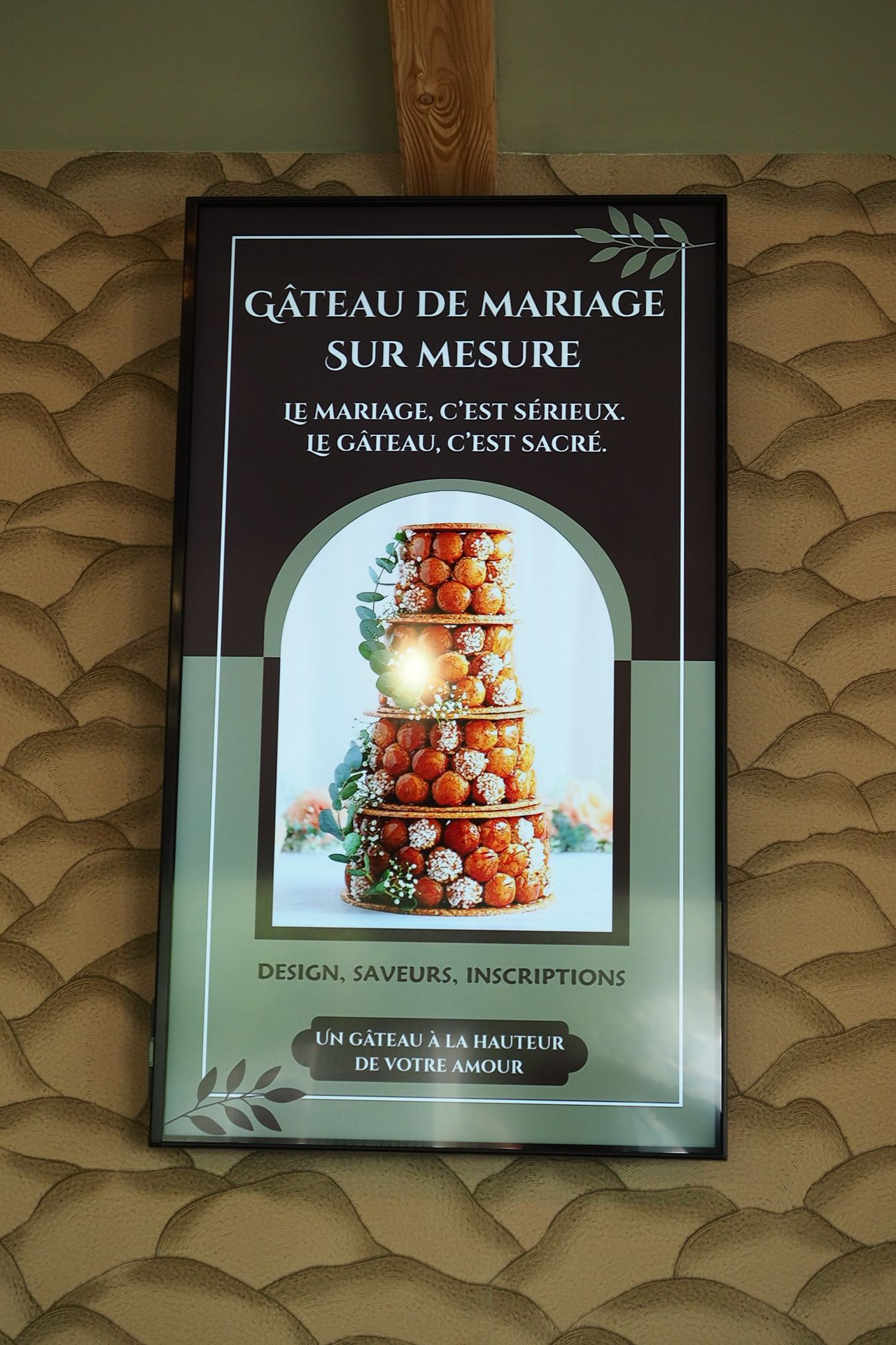 Une pancarte verticale sur un mur à motifs fait la publicité de gâteaux de mariage personnalisés avec une photo d'un croquembouche, en vert et noir.