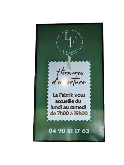 Enseigne verte de La Fabrik indiquant les heures d'ouverture du lundi au samedi, de 7h à 19h, et le numéro de téléphone 04 90 81 17 63.