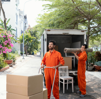 Zwei Personen in orangefarbenen Overalls laden im Freien Möbel und Kartons von einem Umzugswagen ab.