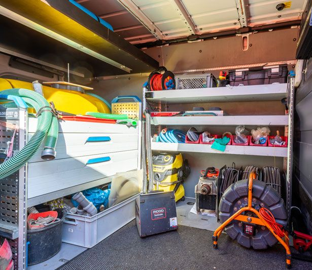 Ein orangefarbenes Spülfahrzeug parkt auf einem gepflasterten Platz. Im Hintergrund sind Gebäude und Bäume zu sehen.