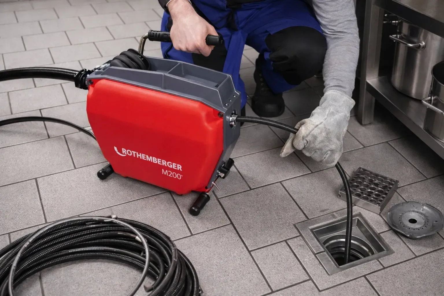 Ein Klempner untersucht mit einer roten Inspektionskamera einen Bodenablauf in einer Großküche.