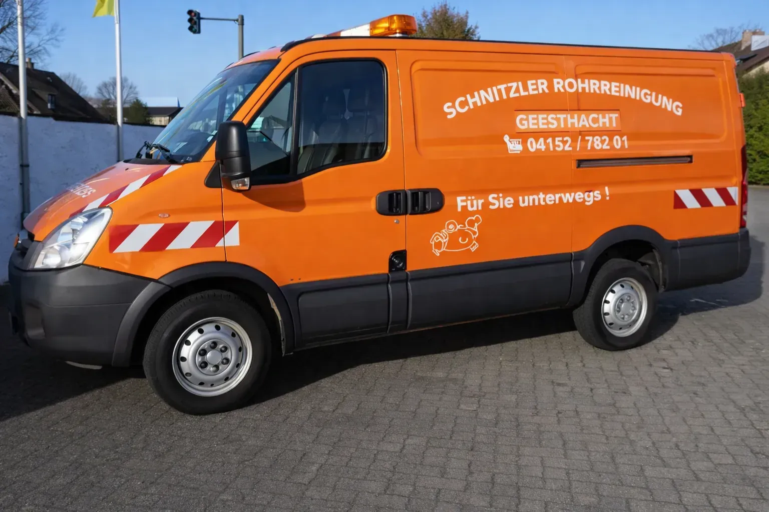 Ein orangefarbener Lieferwagen der Schnitzler Rohrreinigung mit Logo und Telefonnummer parkt auf der Straße.