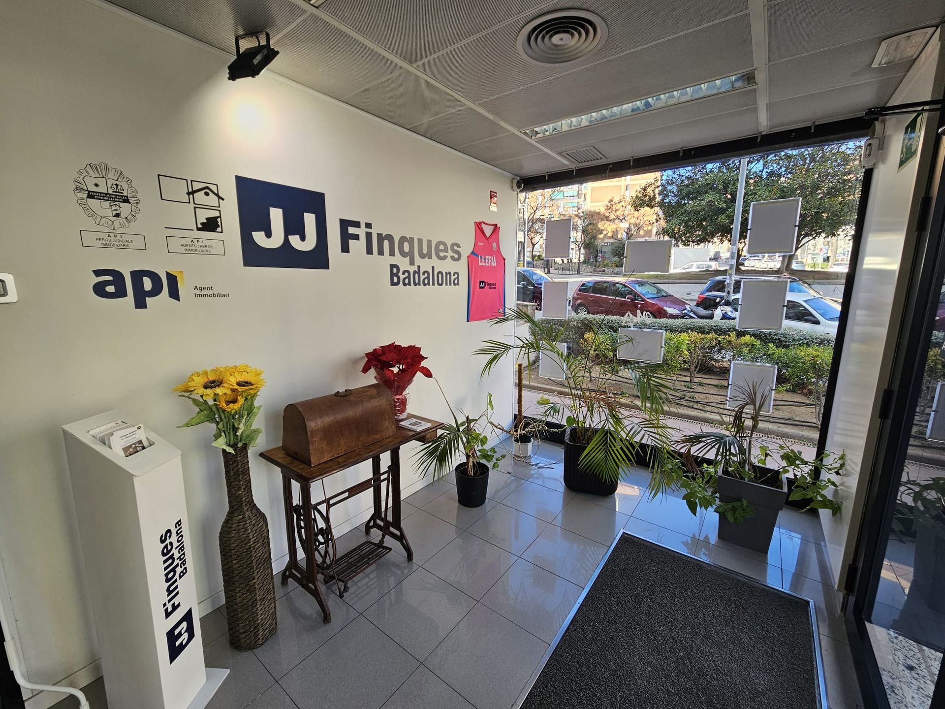 Una habitación con una máquina de coser, jarrones, plantas y un cartel en la pared.