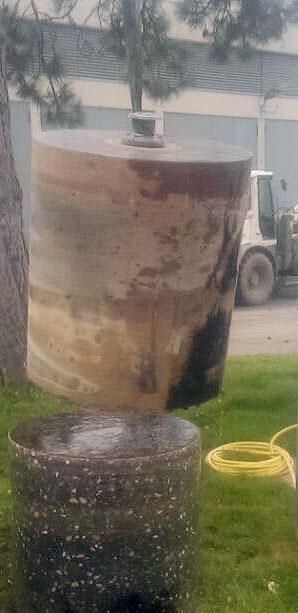 Ein großes Fass steht neben einem Schlauch im Gras.