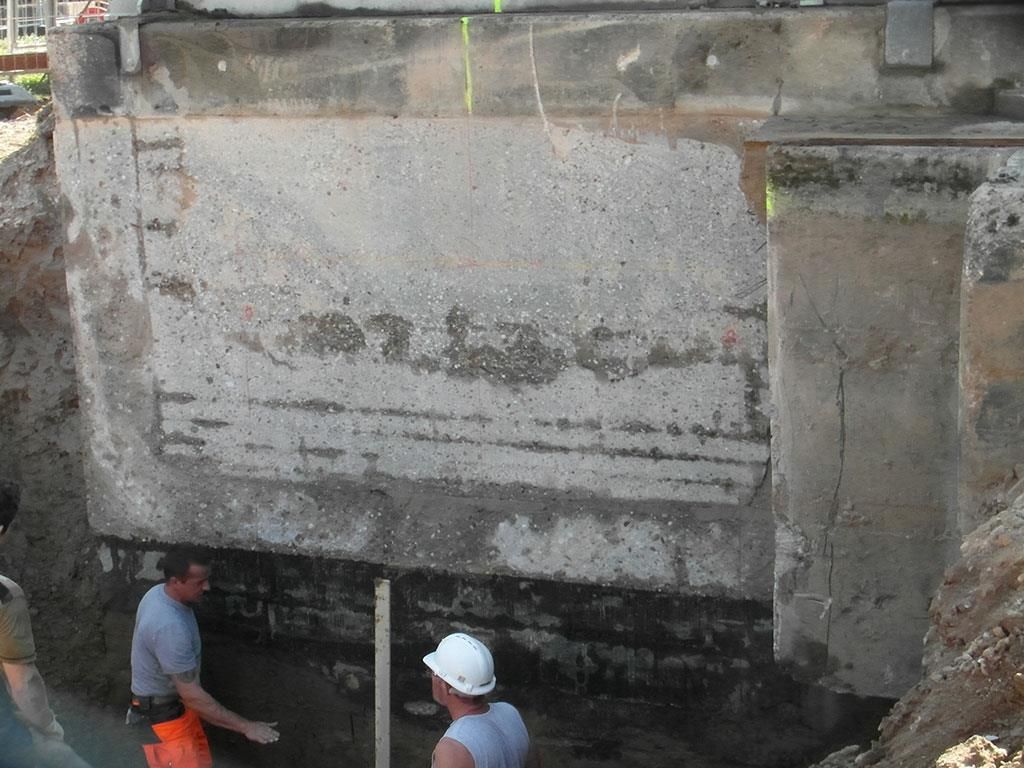 Ein Mann mit Schutzhelm steht vor einer großen Betonmauer
