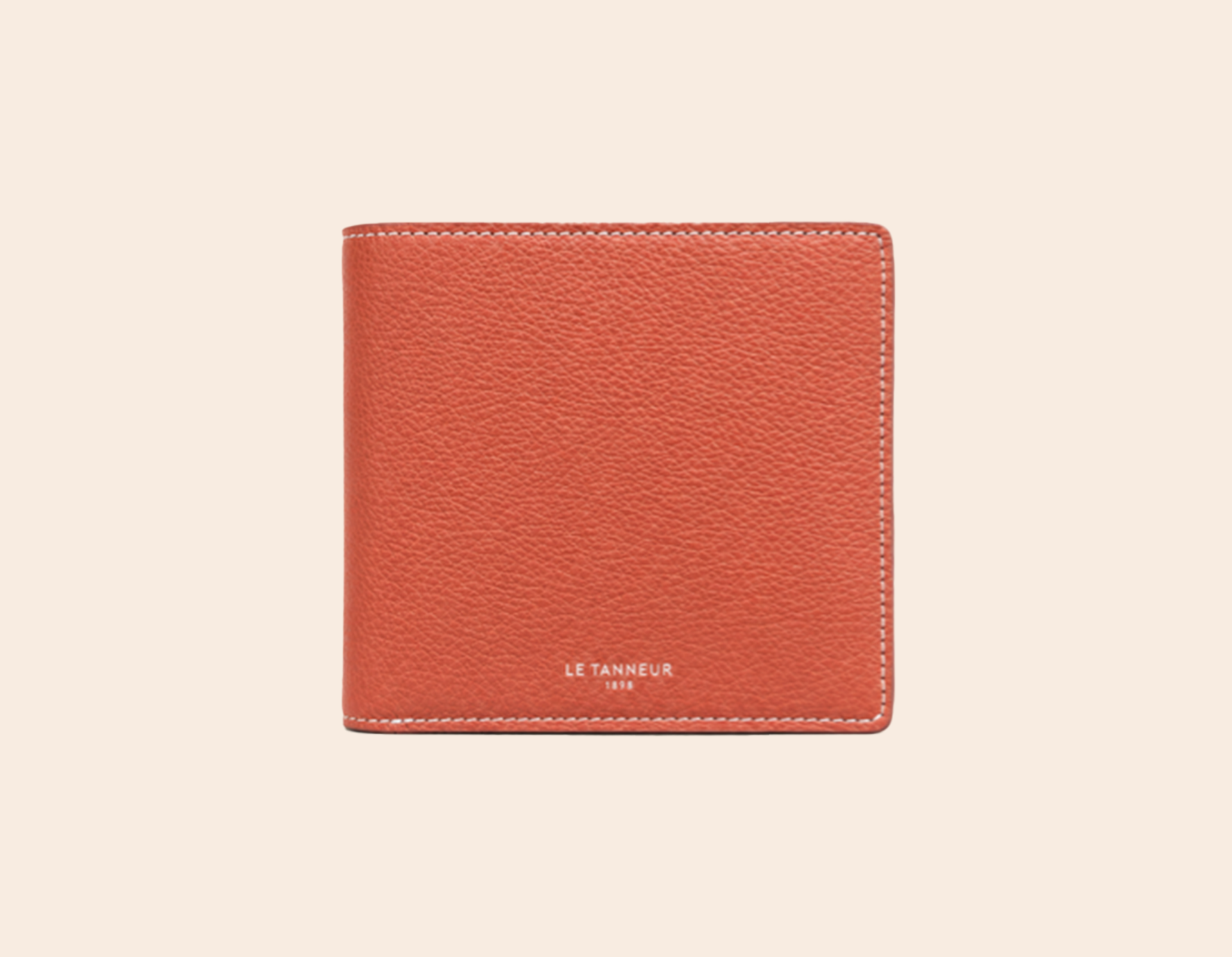 Portefeuille ou porte-cartes en cuir texturé couleur rouille sur fond beige clair.