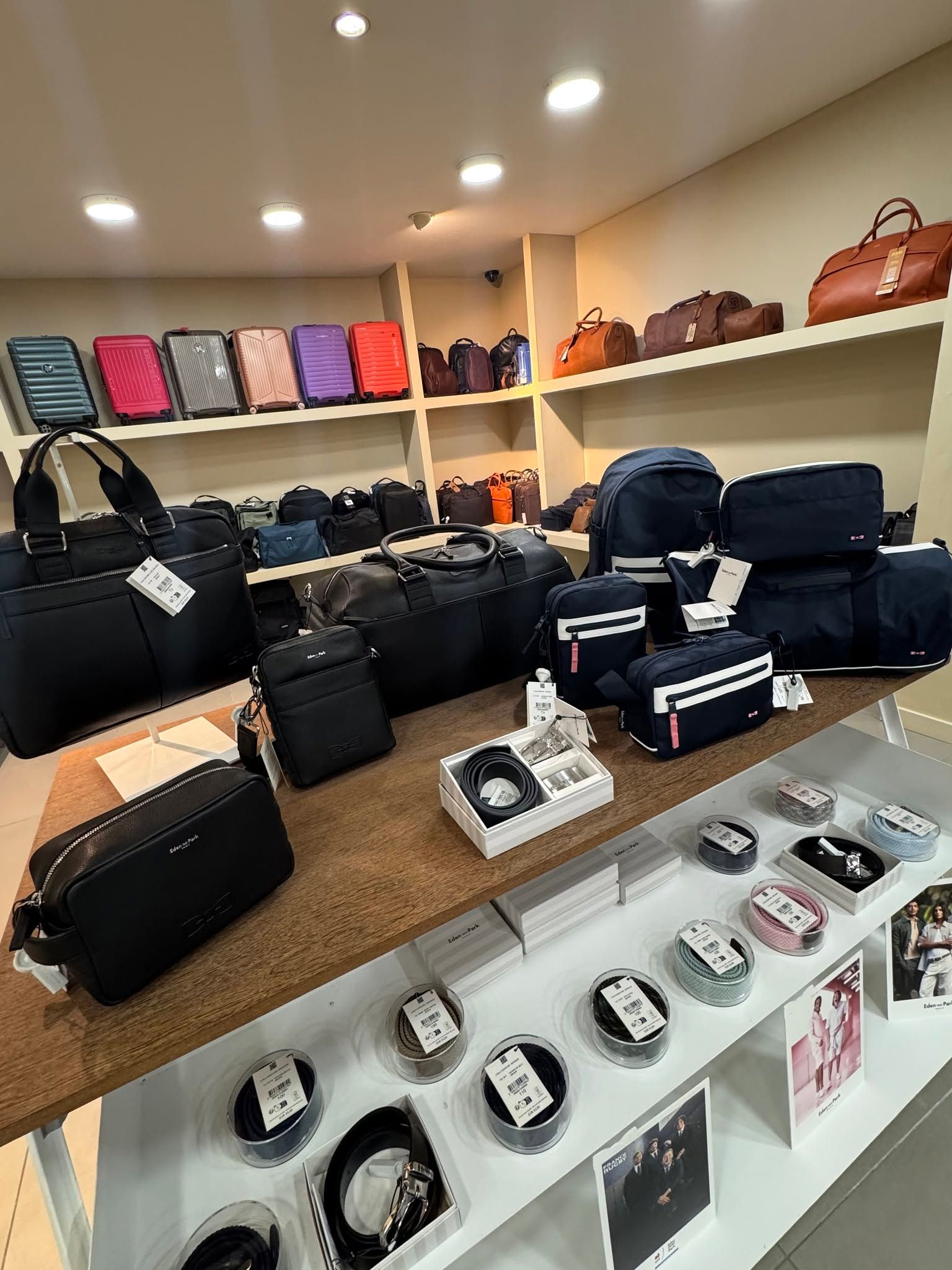 Présentation en magasin de sacs à main noirs, de pochettes colorées et de montres sur les étagères d'une boutique.