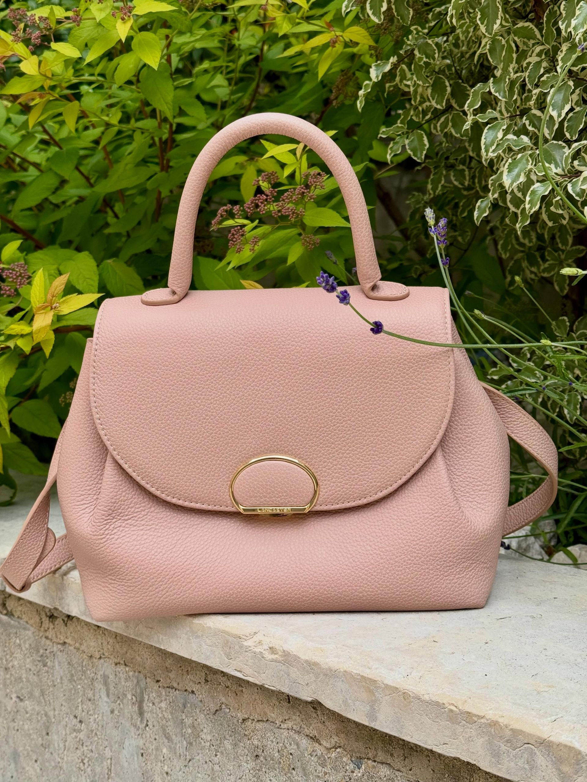 Sac à main rose posé sur un rebord en pierre, avec de la végétation verte en arrière-plan.