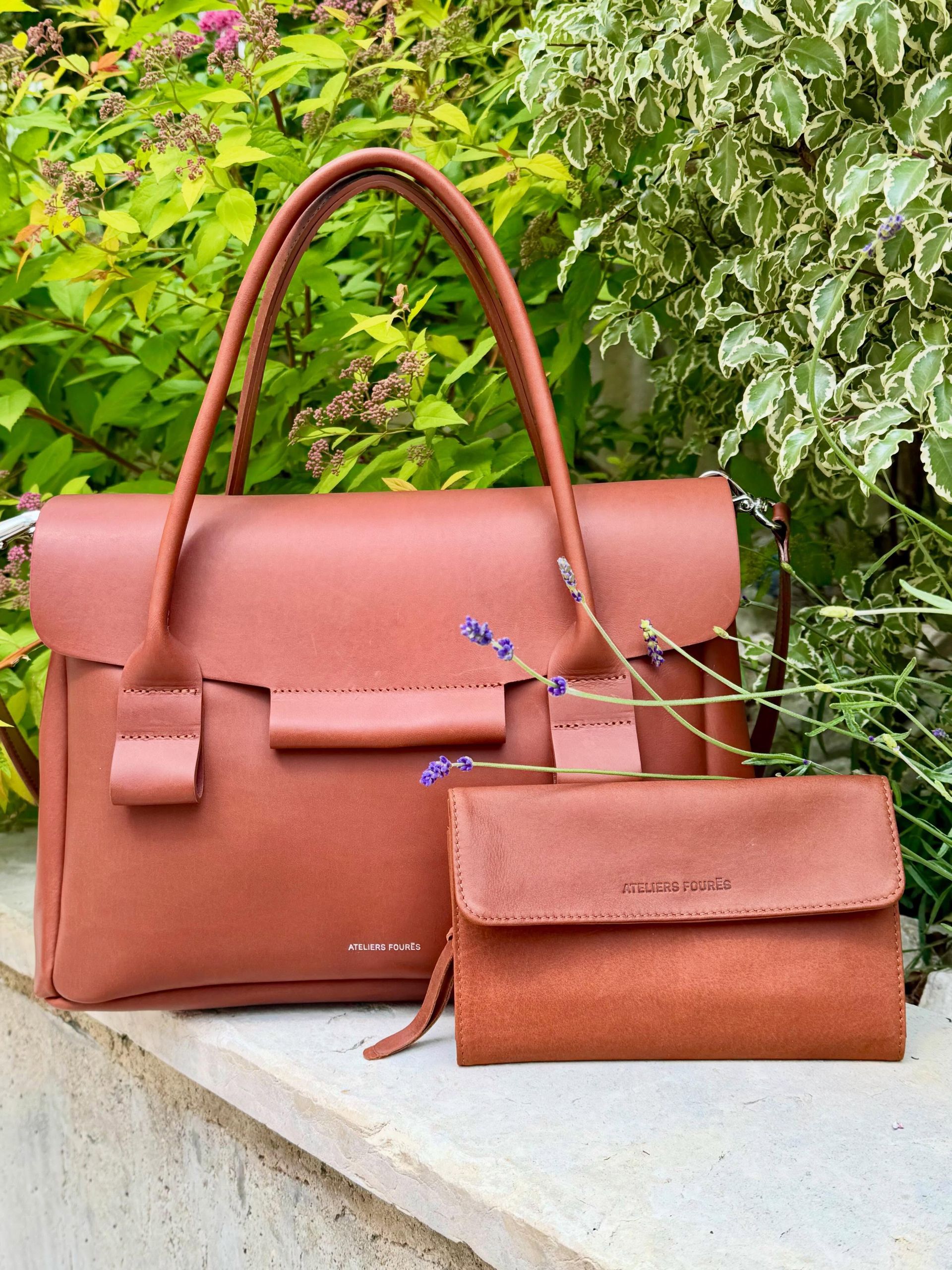 Deux sacs à main en cuir couleur terre cuite posés sur un rebord de pierre, avec de la végétation verte en arrière-plan.