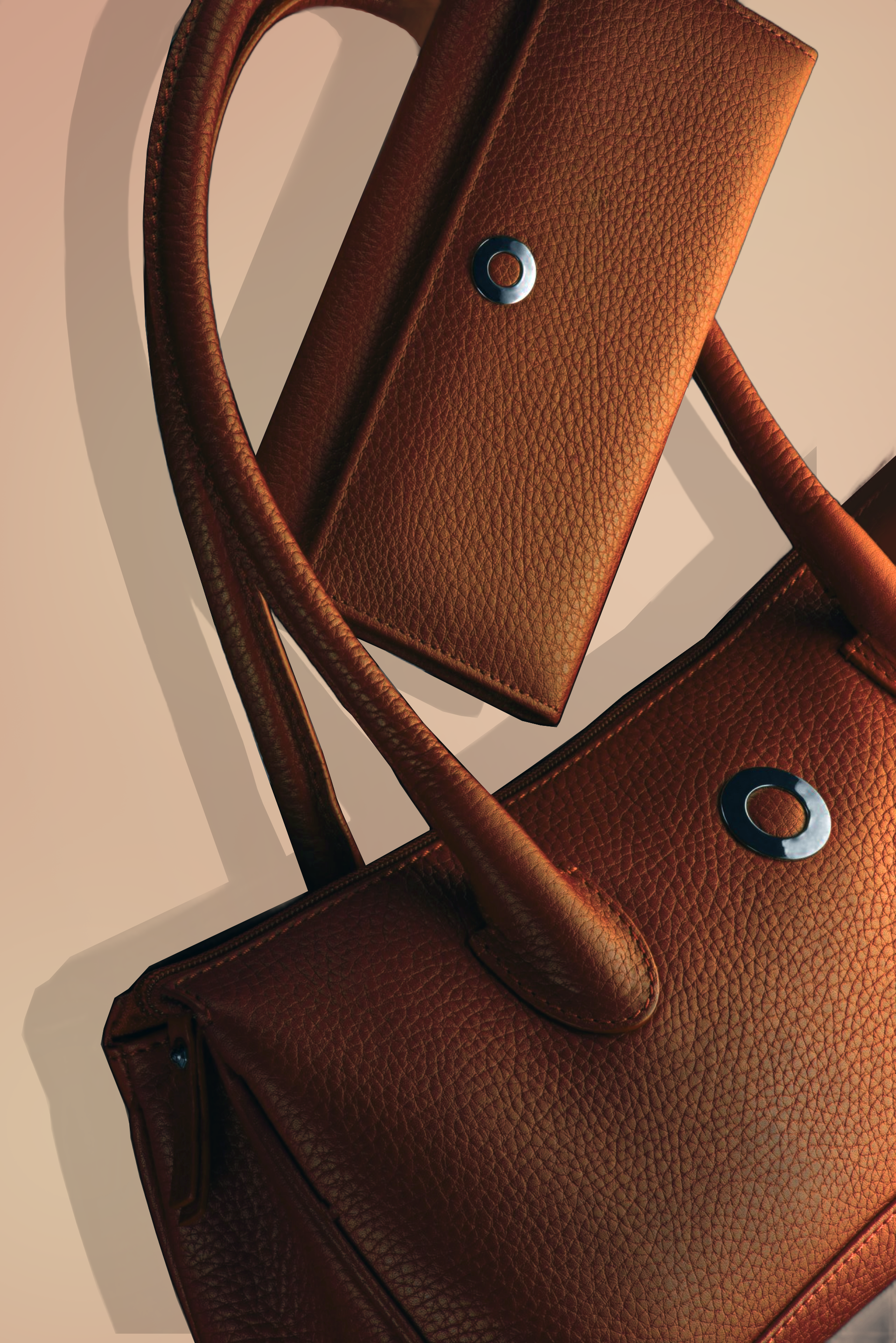 Gros plan sur deux sacs à main en cuir marron avec des anneaux métalliques sur fond beige.
