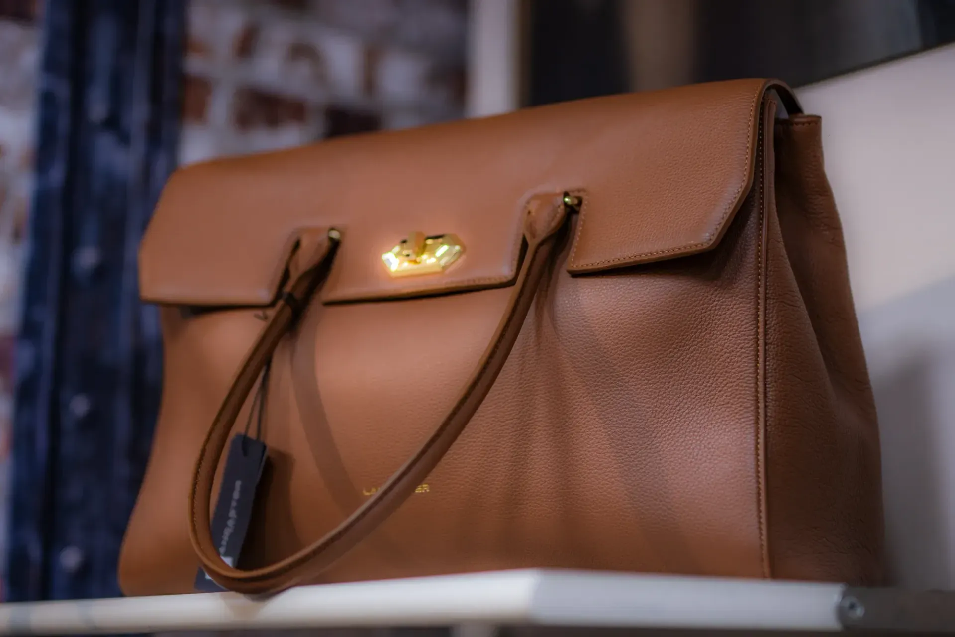 Sac à main en cuir marron sur une étagère, avec fermoir et anses dorés.
