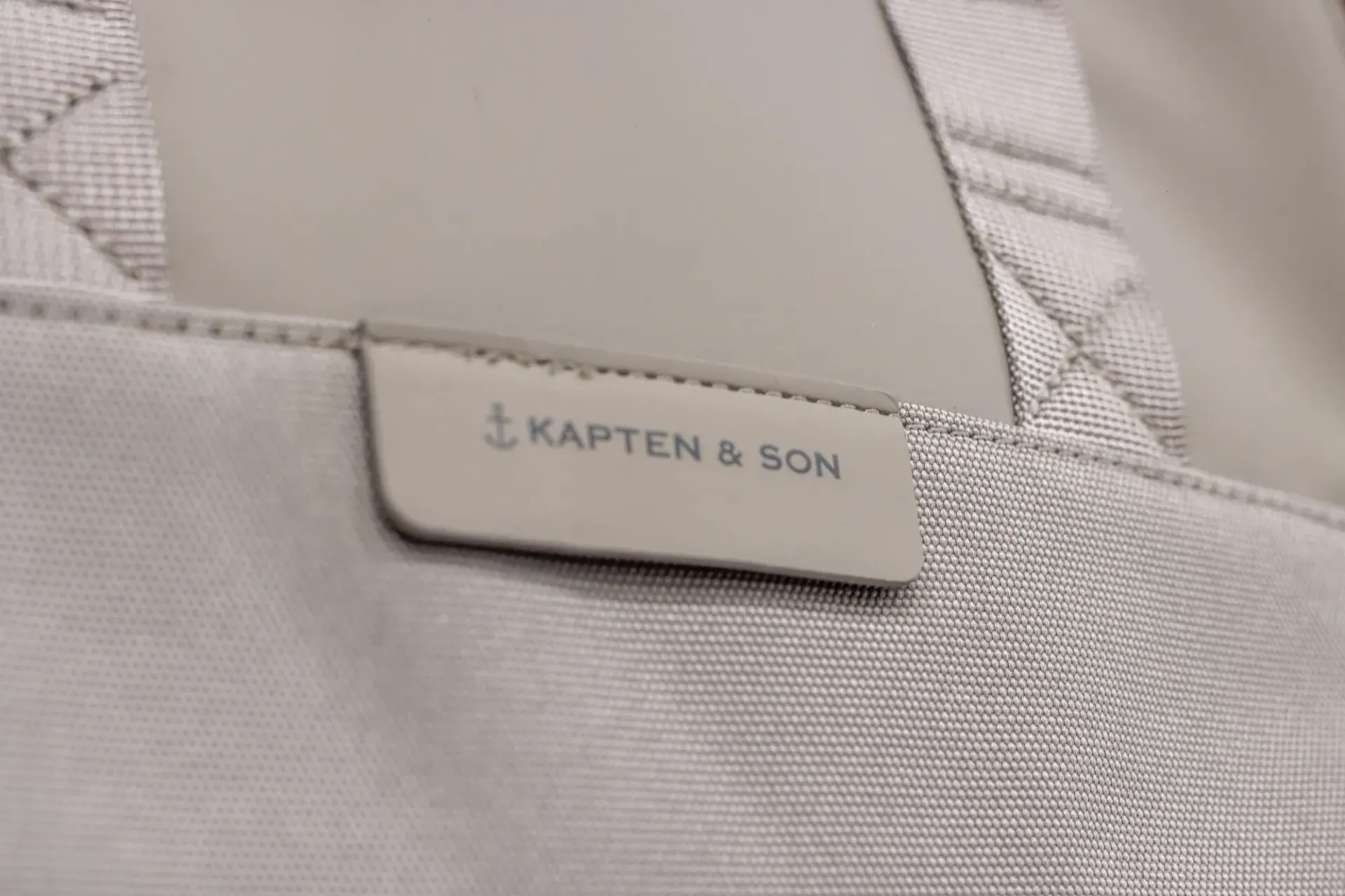 Gros plan sur l'étiquette d'un sac en tissu gris clair portant l'inscription KAPTEN & SON.