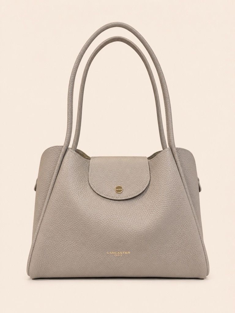 Une personne tenant un sac à main marron, assise sur une chaise blanche et vêtue de vêtements clairs.