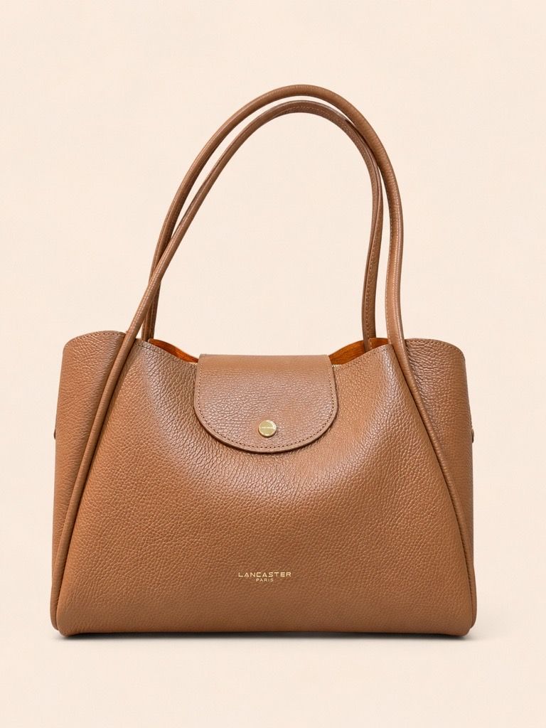 Une personne tenant un sac à main marron, assise sur une chaise blanche et vêtue de vêtements clairs.