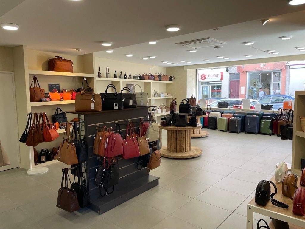 Intérieur lumineux d'un magasin avec des étagères, des sacs à main, des bagages et une table d'exposition en bois près de la vitrine.