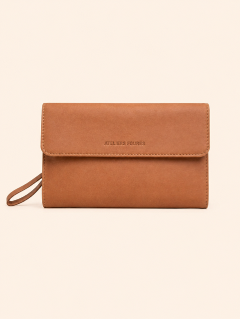 Une personne portant une robe beige et tenant une pochette dorée à l'extérieur, sous une douce lumière du soleil.