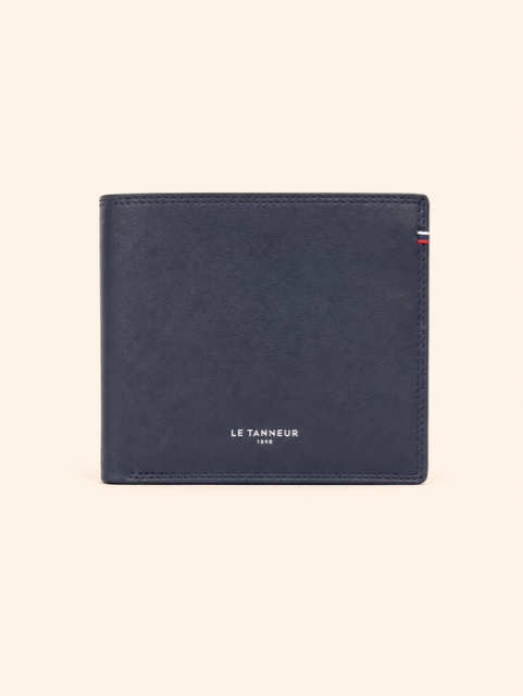 Une femme se tient debout à l'intérieur, tenant une pochette beige, à côté d'étagères blanches.