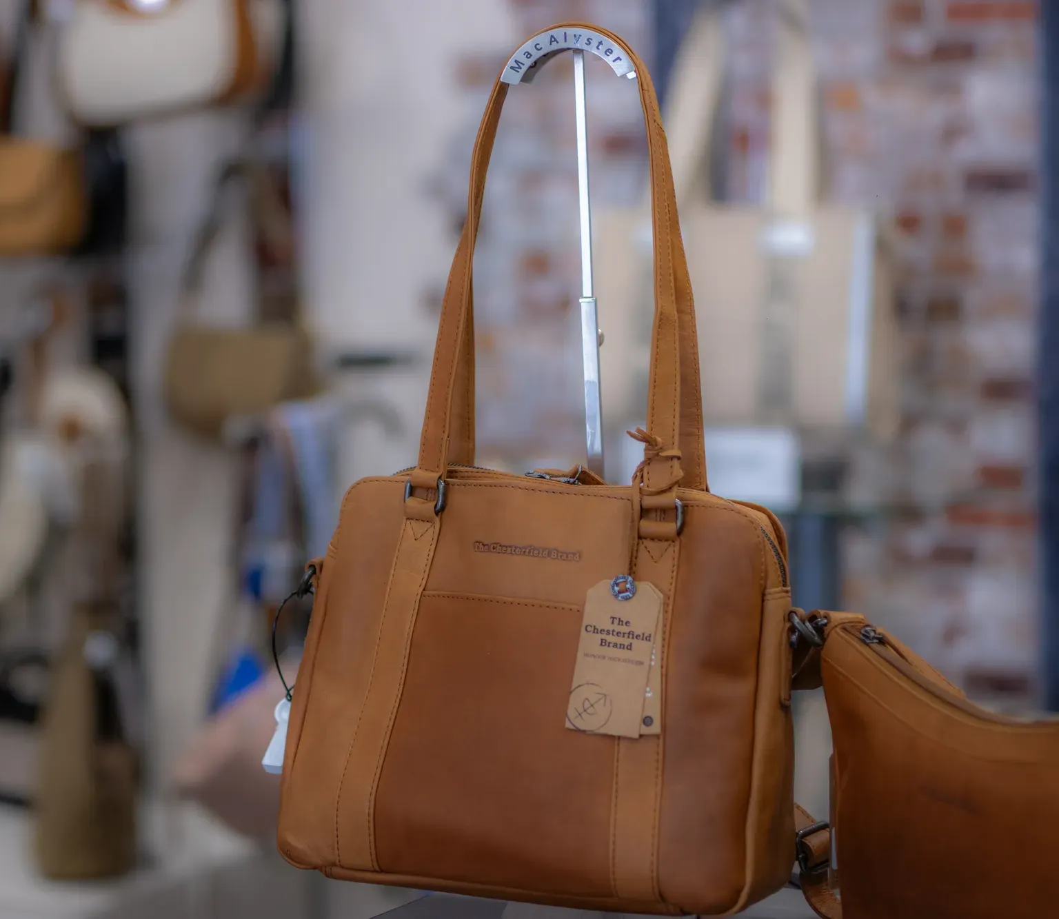 Sac cabas en cuir marron avec de longues anses et une étiquette suspendue, exposé sur une étagère de magasin.