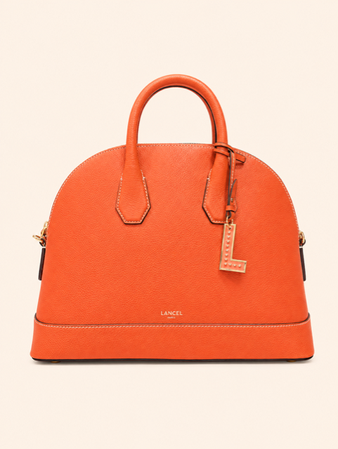 Sac à main en cuir orange avec poignée supérieure et breloque lettre dorée sur fond beige