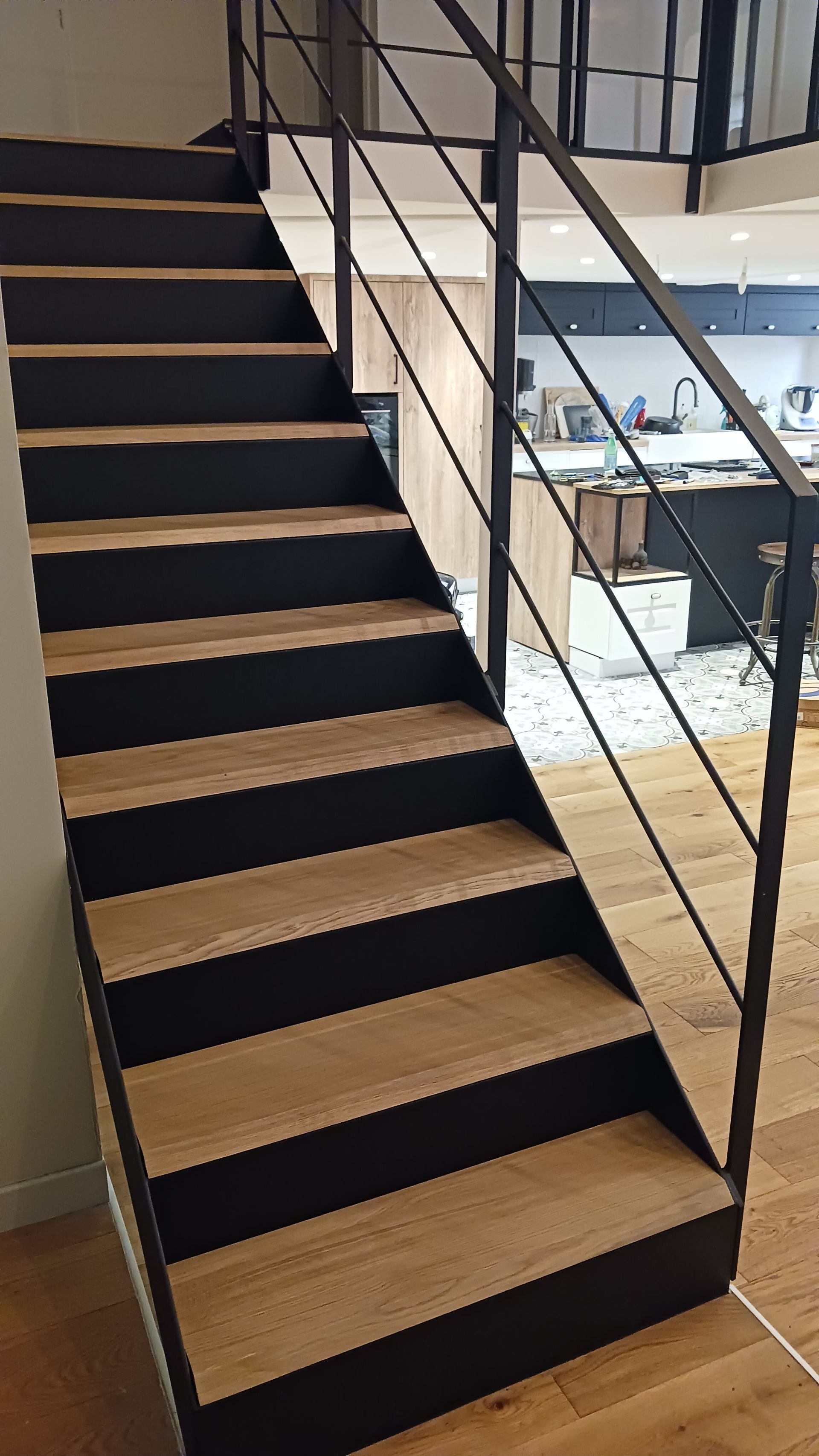 Escalier en bois aux côtés noirs et à la rampe en métal, menant vers l'étage.