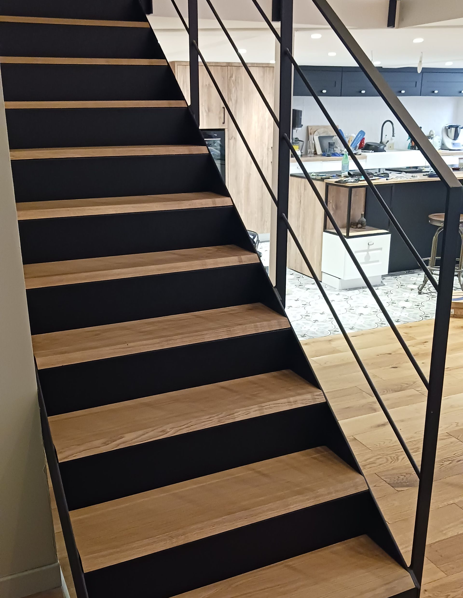 Escalier en bois avec côtés noirs et rampe en métal dans une maison moderne.