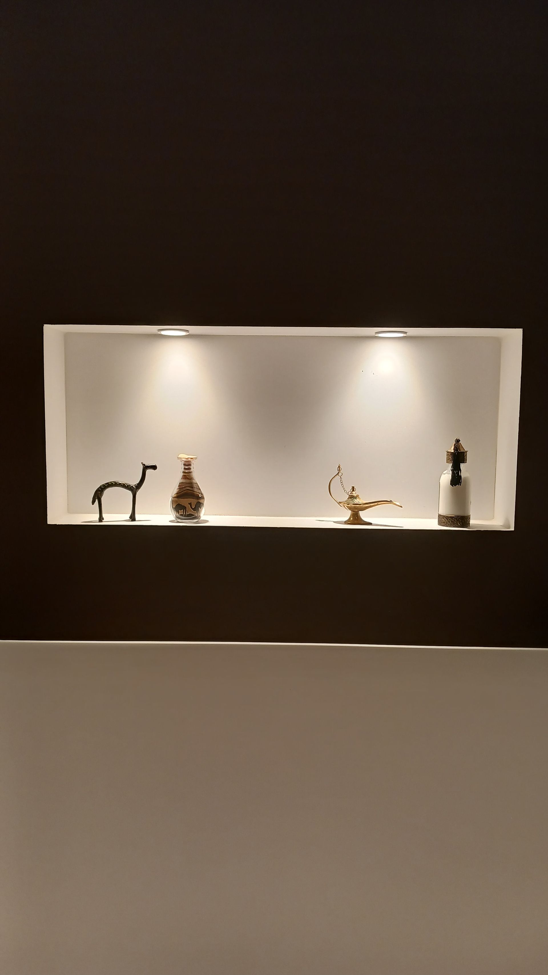 Étagère murale encastrée avec quatre objets décoratifs, éclairée par deux spots.