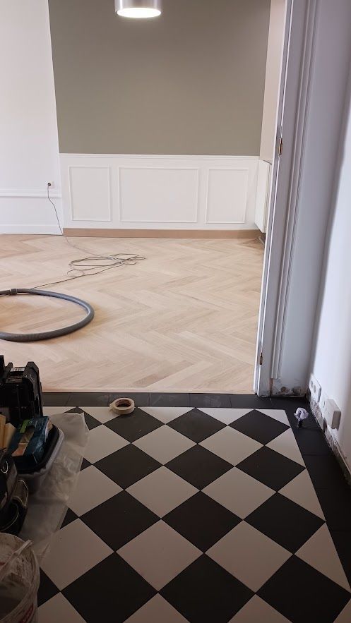 Pièce avec un sol à damier noir et blanc menant à un parquet en chevrons et des panneaux muraux blancs.