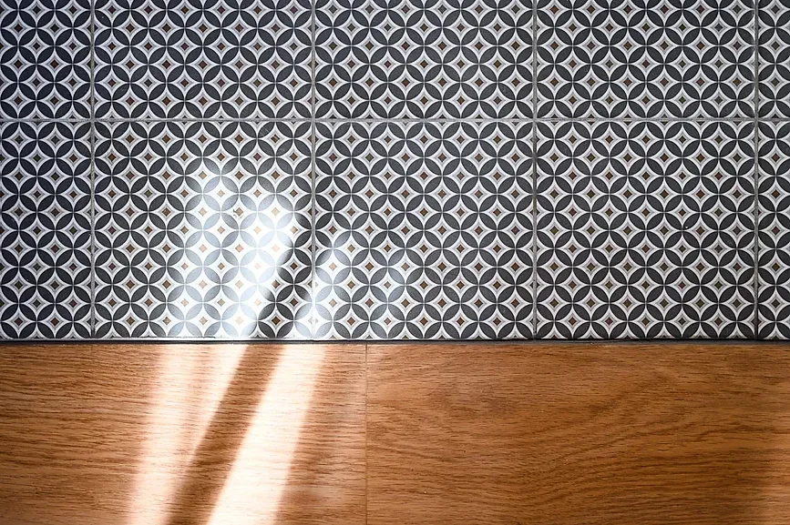 Sol carrelé de carreaux géométriques gris et blancs au-dessus d'un parquet.